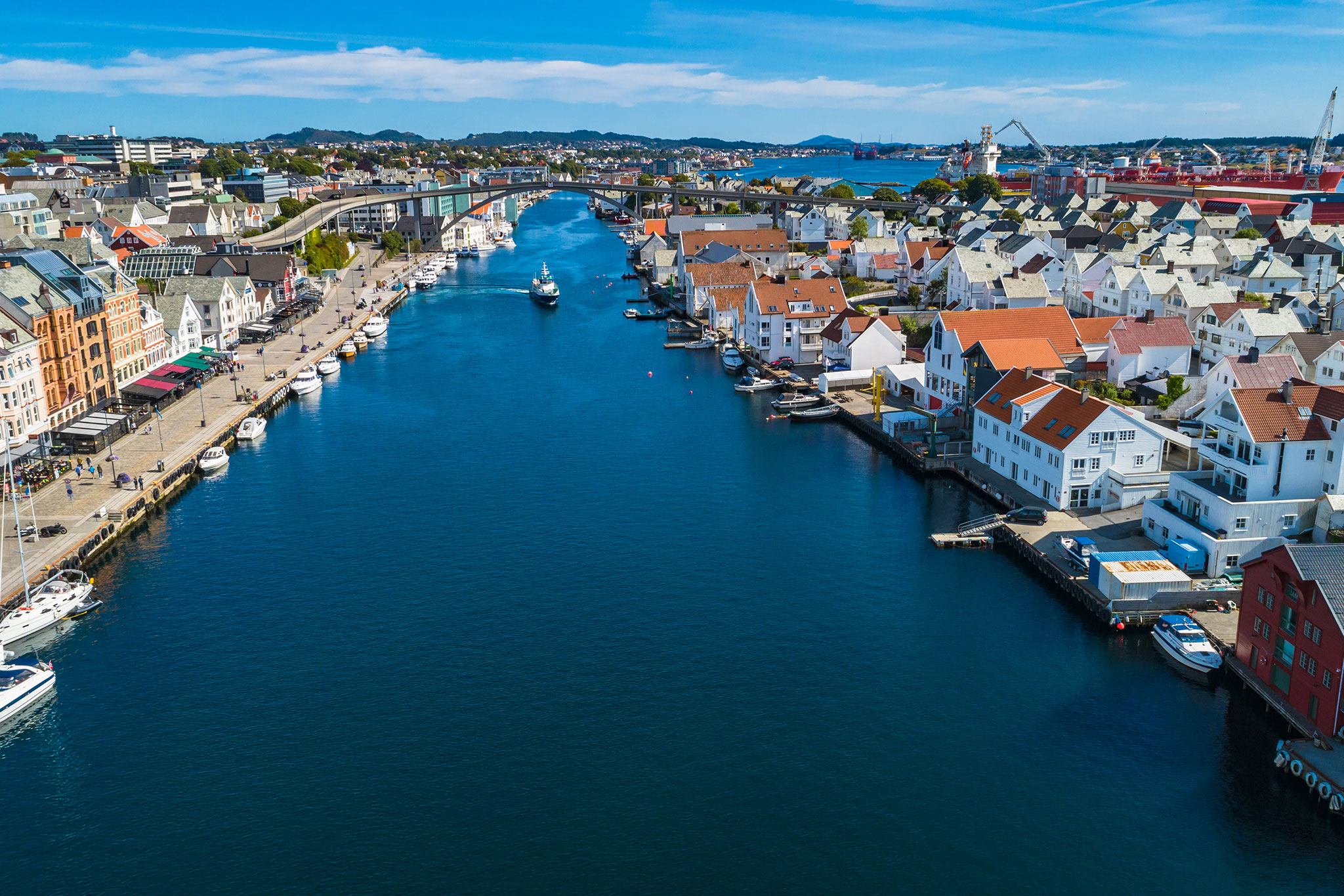 Aerial view of Haugesund, Norway, showing colorful waterfront buildings, boats docked along the canal and clear blue water under a bright sky.
