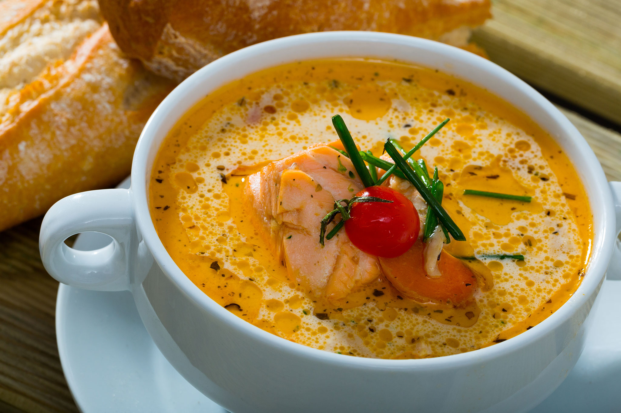 Bowl of creamy Norwegian fish soup with salmon, cherry tomato, herbs and bread on the side.