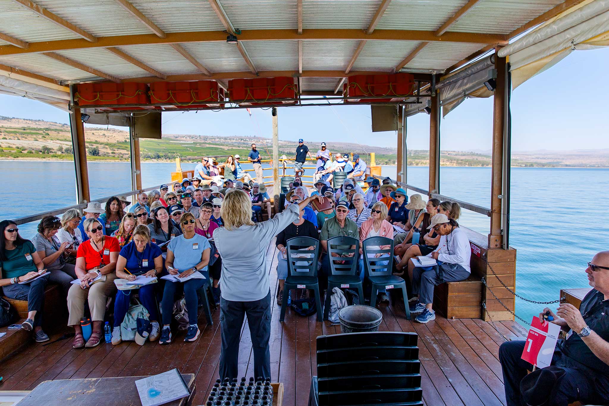 A group listens to a speaker aboard a covered boat while sailing on the Sea of Galilee.