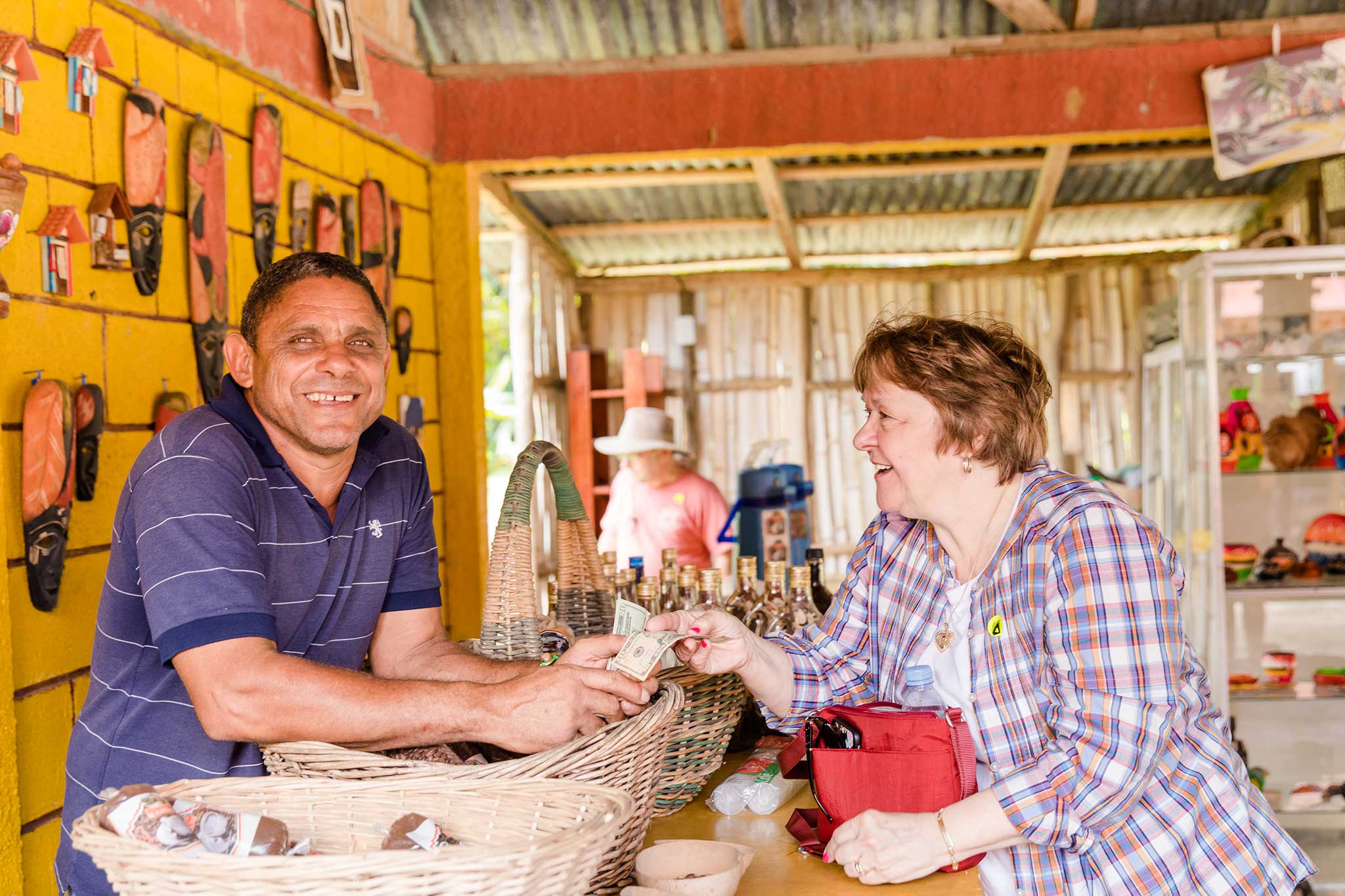 A traveler smiles while purchasing handmade goods from a local vendor at a colorful artisan market, sharing a friendly moment during their visit.