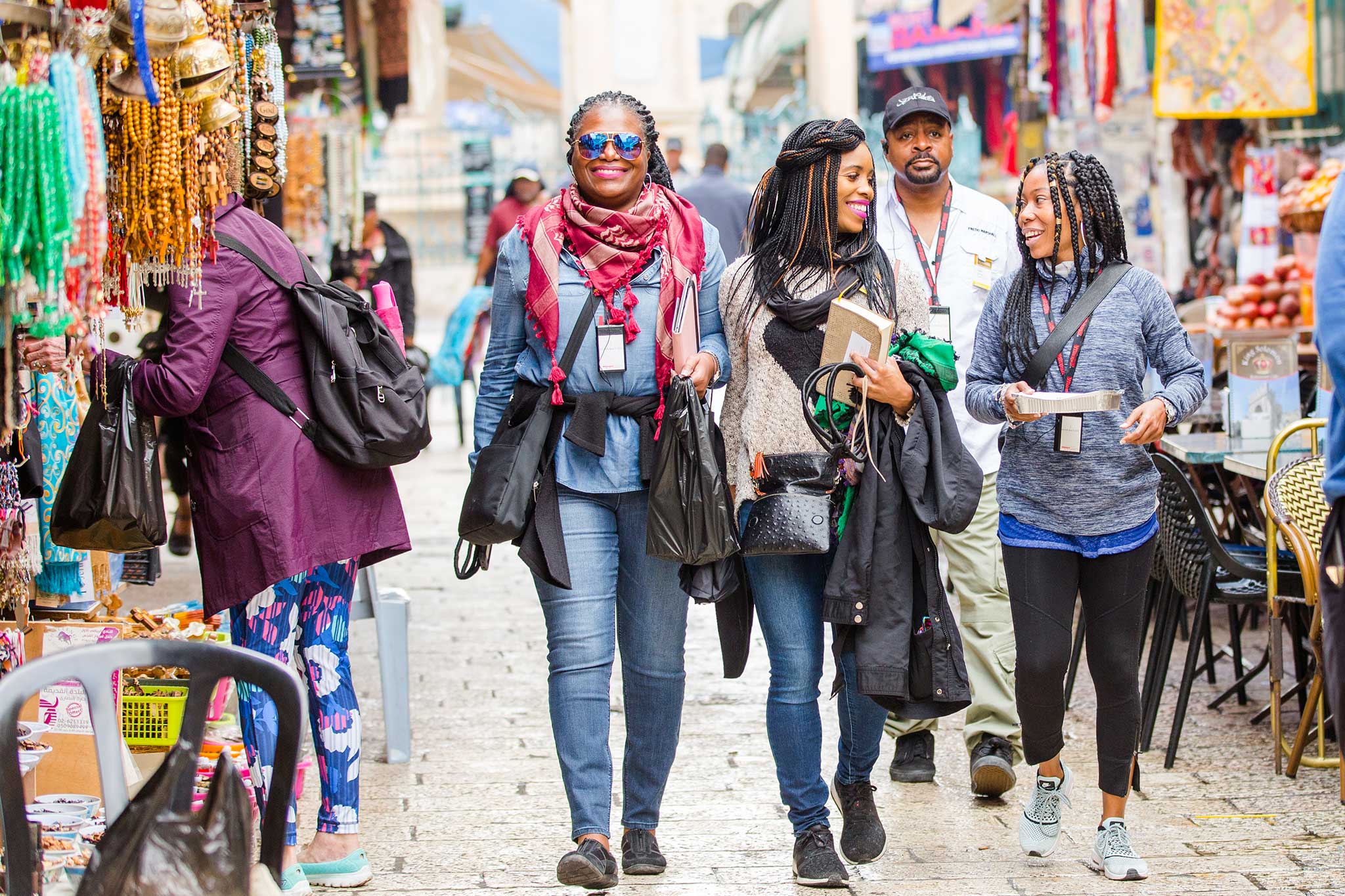 A group of travelers stroll through a bustling outdoor market lined with colorful shops and handmade goods, enjoying the lively atmosphere as they explore together.