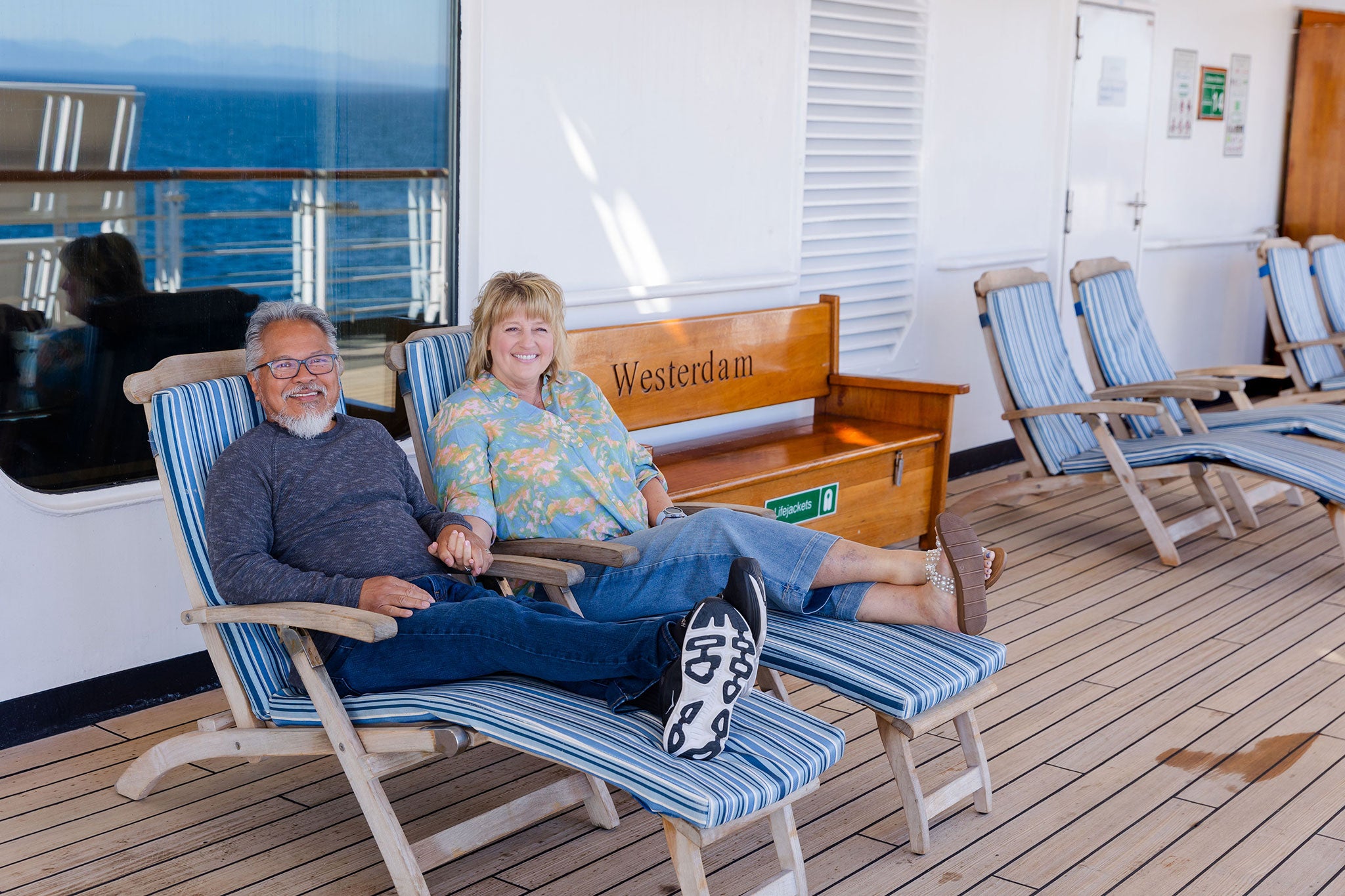 Older couple relaxing on blue deck chairs in a ship’s outdoor lounge.