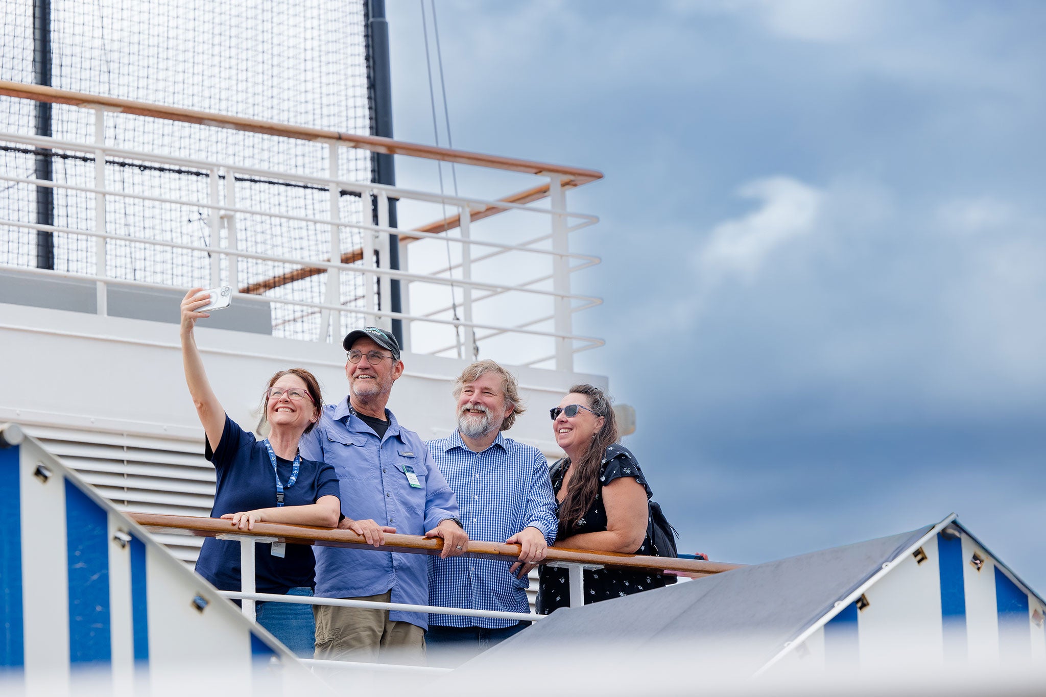 Four people on a boat deck taking a selfie, blue sky behind