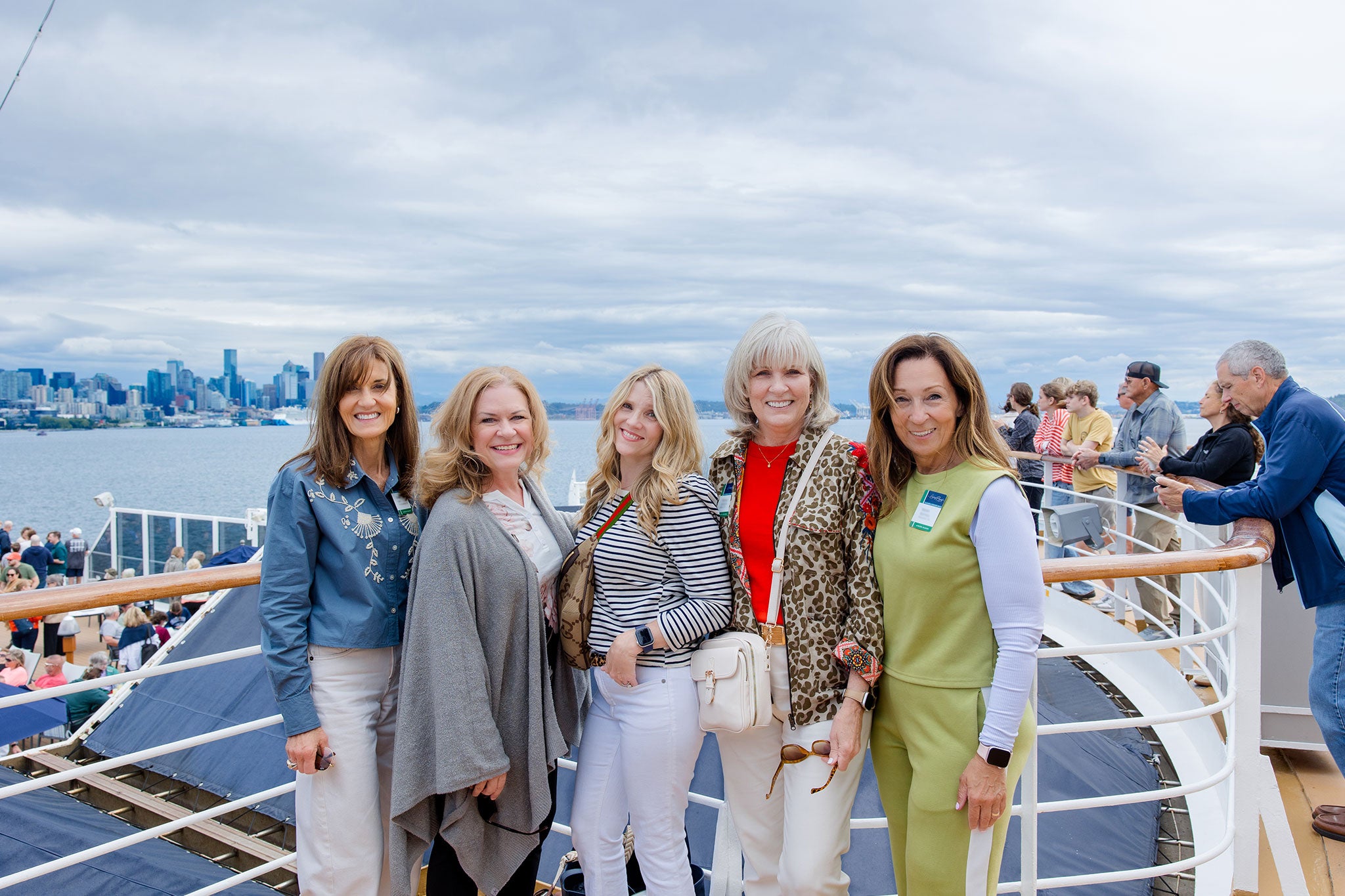 Five women smiling on a ship deck, with ocean and cloudy sky behind them.