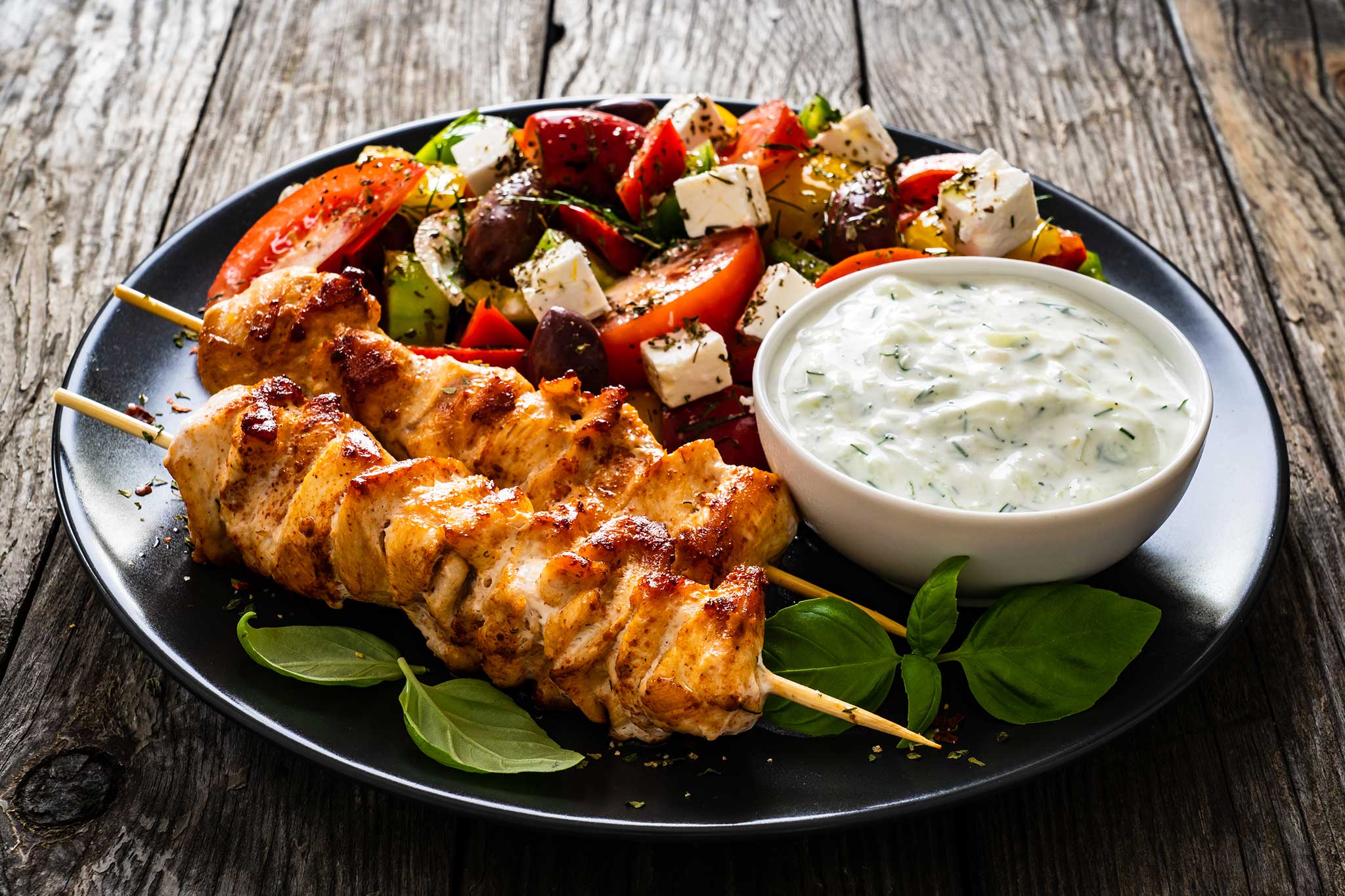 Plate of grilled chicken skewers, salad, and dipping sauce on rustic table