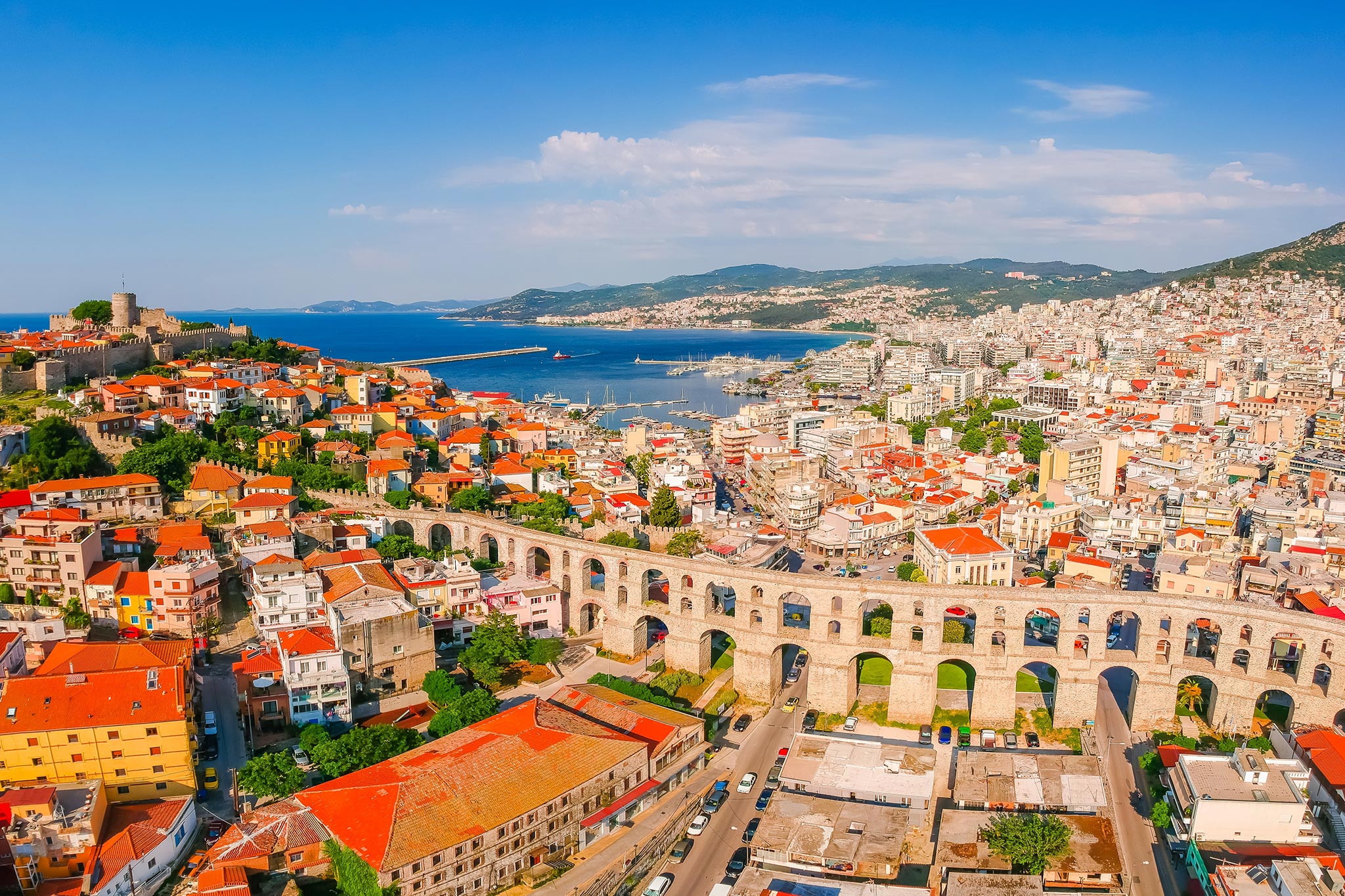 Aerial view of a coastal city with colorful rooftops and a large stone aqueduct