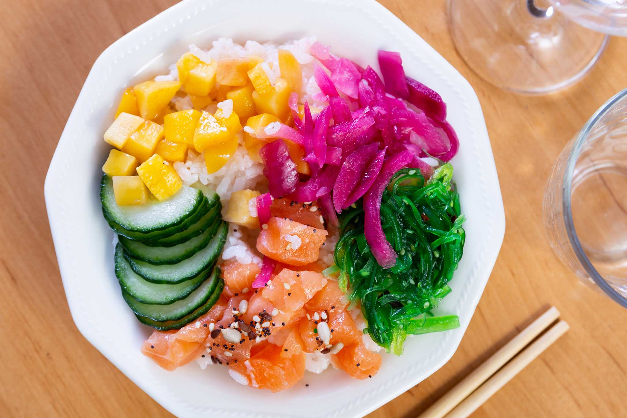 Bowl of salmon poke with cucumber, mango, seaweed salad, egg, and pickled cabbage