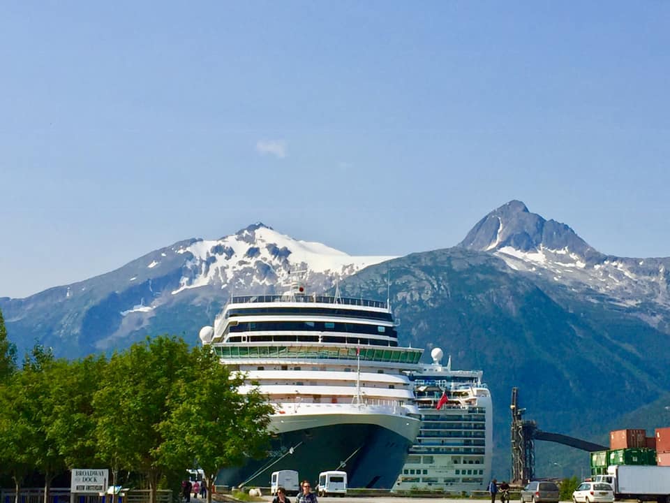 Front of a cruise ship with snow capped mountains behind it