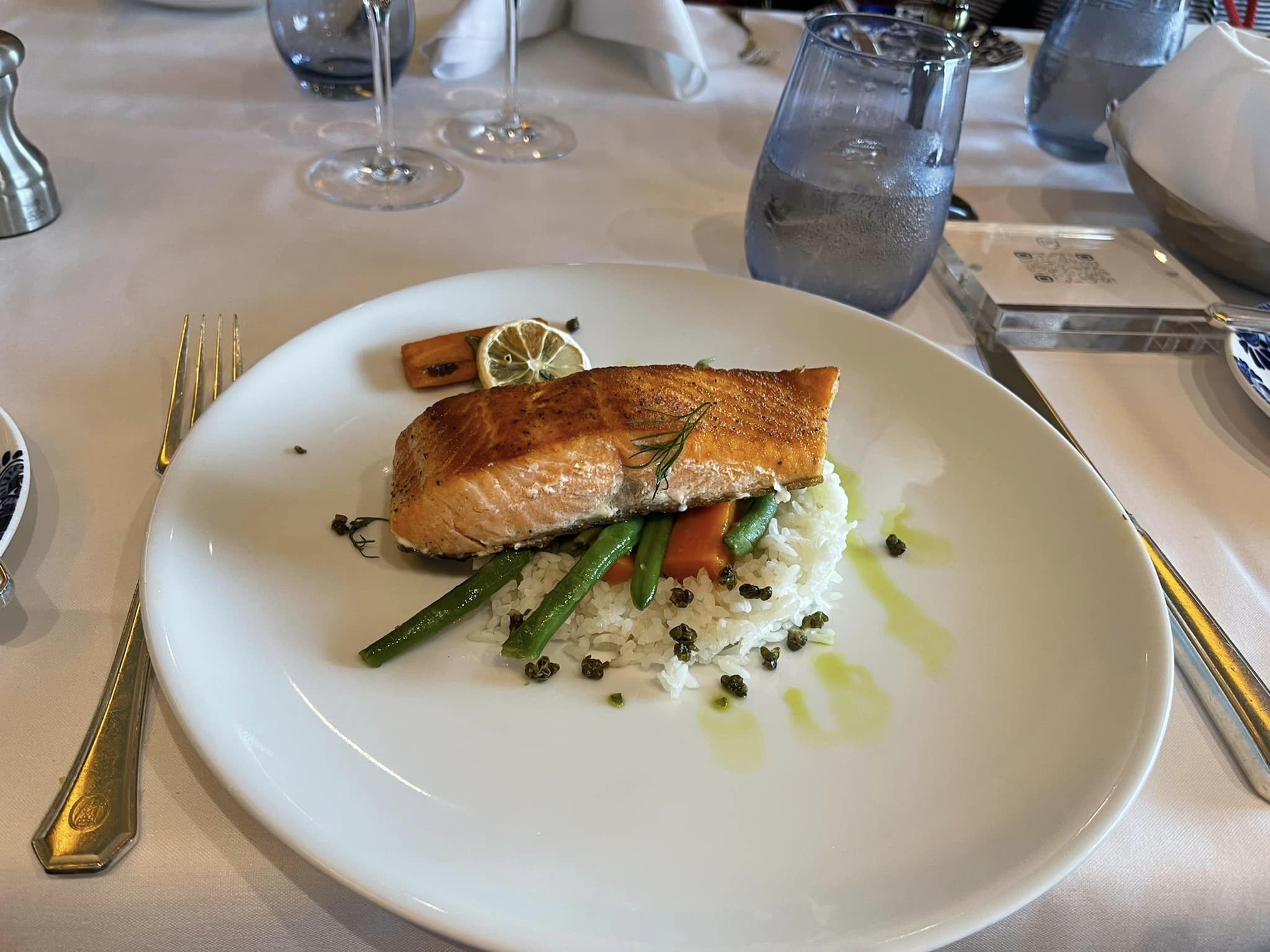 Baked salmon with rice and vegetables on a white plate set on an elegant table
