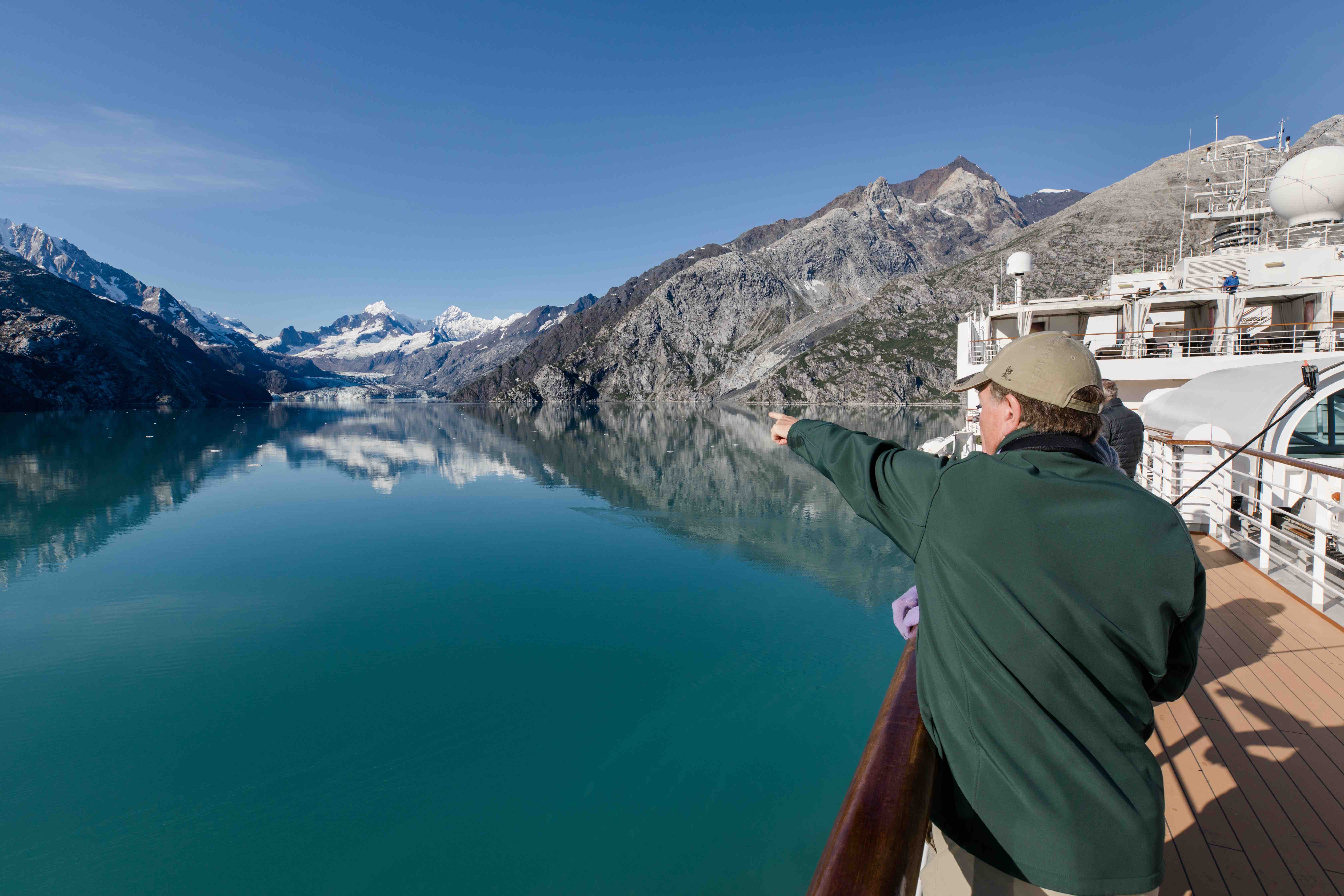 Man in a green jacket standing on the ship deck, pointing at Glacier Bay.