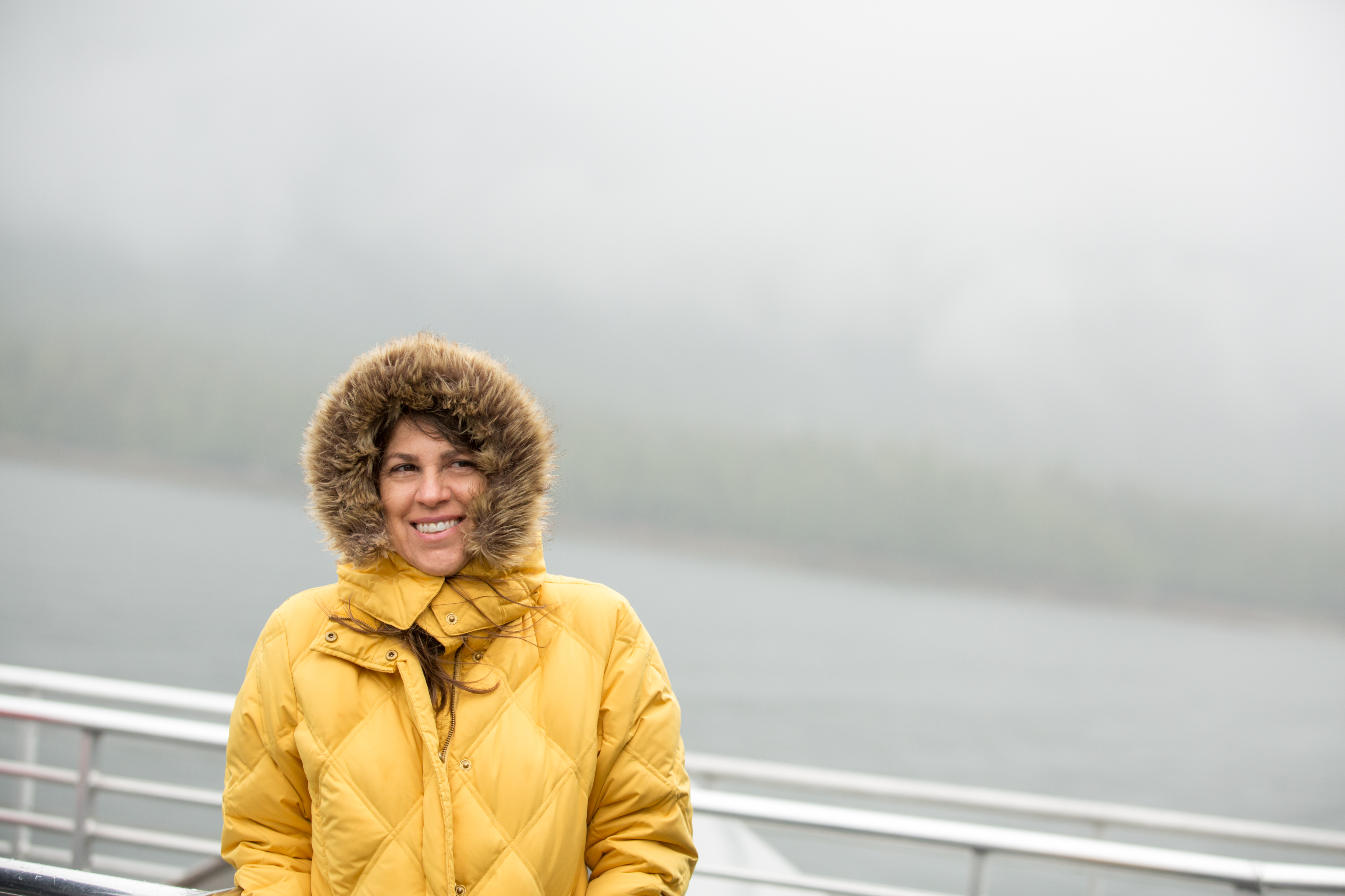 Woman wears a yellow fur-lined jacket on misty boat ride