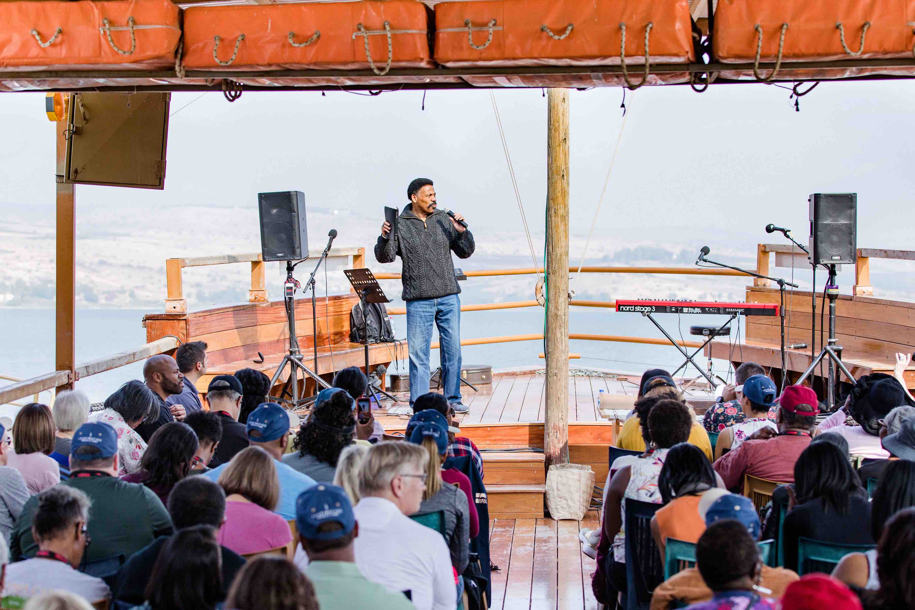 Tony Evans holding the Bible and preaching to a group of people on a first-century replica boat on the Sea of Galilee