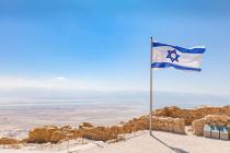 Israeli flag waving on top of the rocky Masada fortress overlooking the desert.