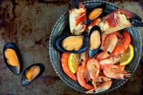 A bowl full of crab claws, clams, shrimp and lemons