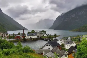 Norwegian fjord village with colorful houses, waterfront buildings, and steep mountains under cloudy skies.