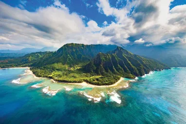 Aerial photo of lush mountainous island with turquoise lagoon and reef under cloudy sky