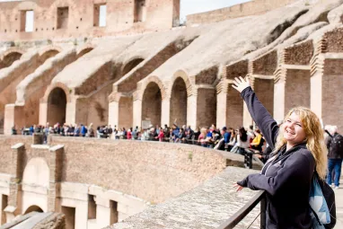 Woman posing by railing inside the Colosseum, with arches and tourists in the background.