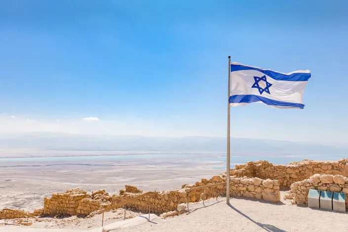 Israeli flag waving on top of the rocky Masada fortress overlooking the desert.