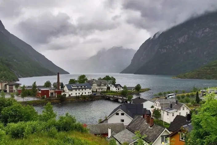 Norwegian fjord village with colorful houses, waterfront buildings, and steep mountains under cloudy skies.