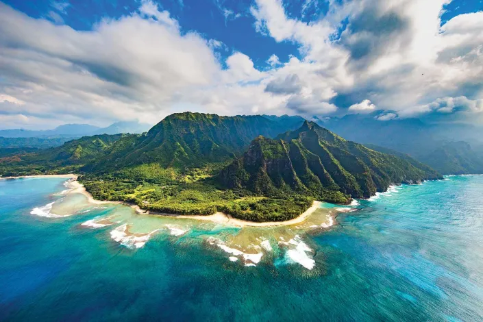Aerial photo of lush mountainous island with turquoise lagoon and reef under cloudy sky