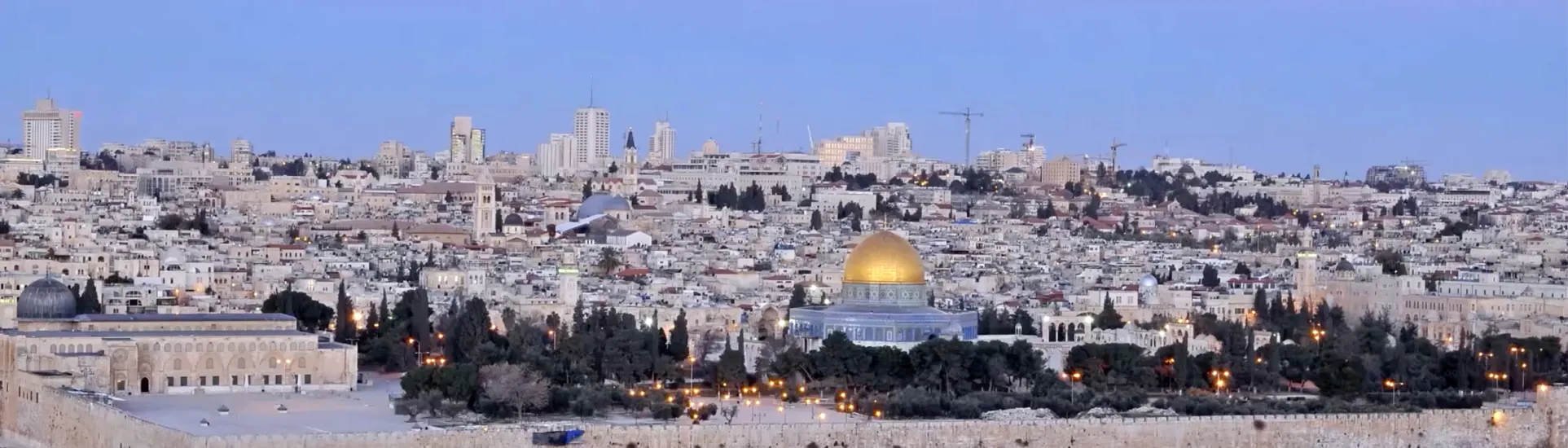 Panoramic view of Jerusalem at dusk, featuring the golden Dome of the Rock surrounded by the historic city skyline and illuminated landmarks.