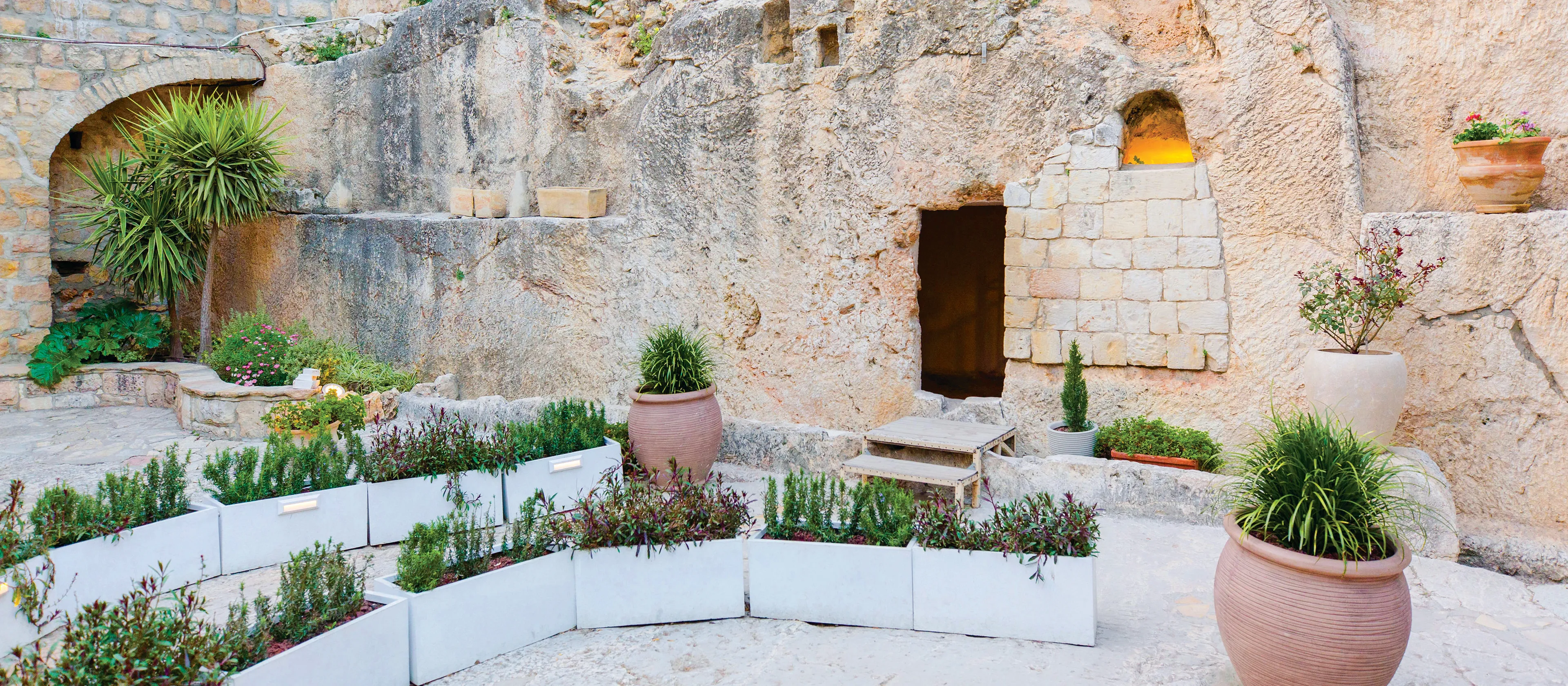 Entrance to the Garden Tomb surrounded by white planters, and potted greenery