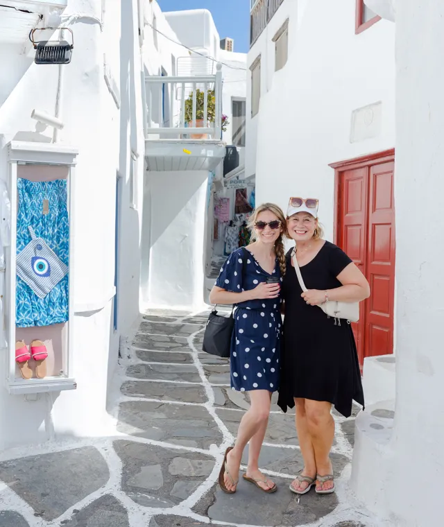 Two smiling women standing together on a street in Mykonos