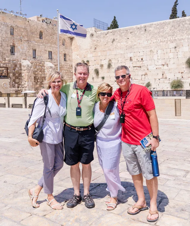 A group of travelers standing together with an Israeli flag and the Western Wall in the background