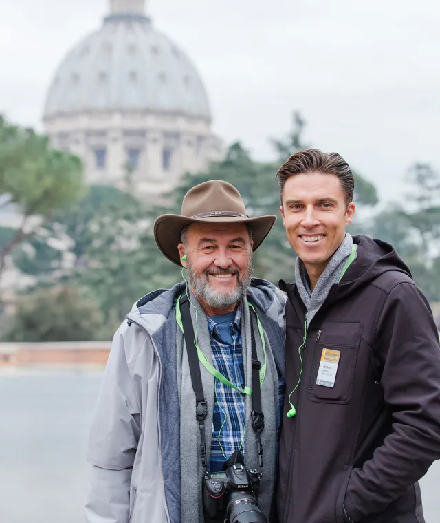Two tour guests smiling in front of St. Peter's Basilica in Rome, Italy