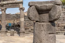 Ancient basalt stone ruins at Chorazin in Galilee, featuring carved columns and archaeological remains of a first-century synagogue beneath a blue sky.