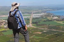 Traveler standing atop Mount Arbel overlooking the Sea of Galilee, with sweeping views of the surrounding countryside, farmland, and shoreline below.