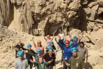 Group of adventurers wearing helmets posing at the entrance to Malcham Cave near the Dead Sea, surrounded by towering desert rock formations.