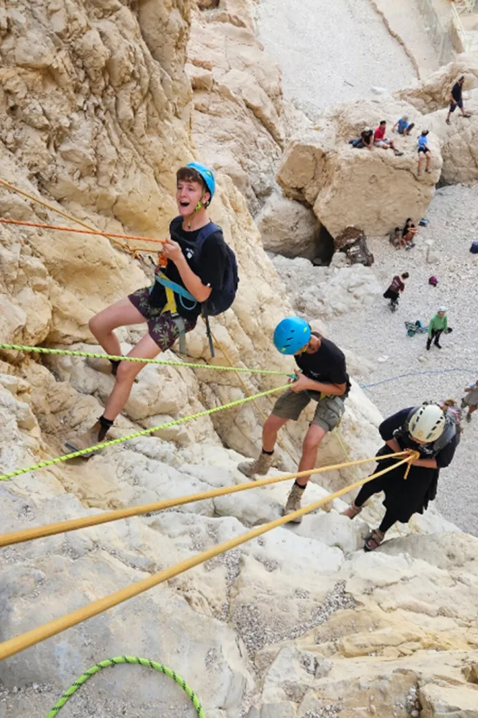 Participants rappelling down the limestone cliffs of Nahal Tamar near the Dead Sea, wearing helmets and harnesses during a guided desert adventure.