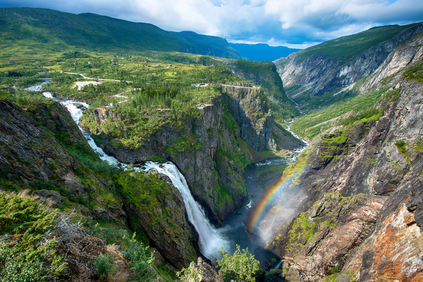 A large waterfall going down into a valley surrounded by green mountains
