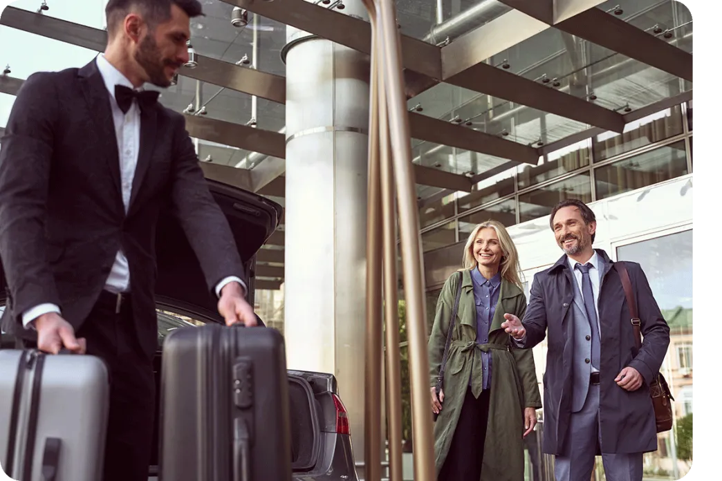 Hotel staff member carrying luggage as a smiling couple arrives at the entrance
