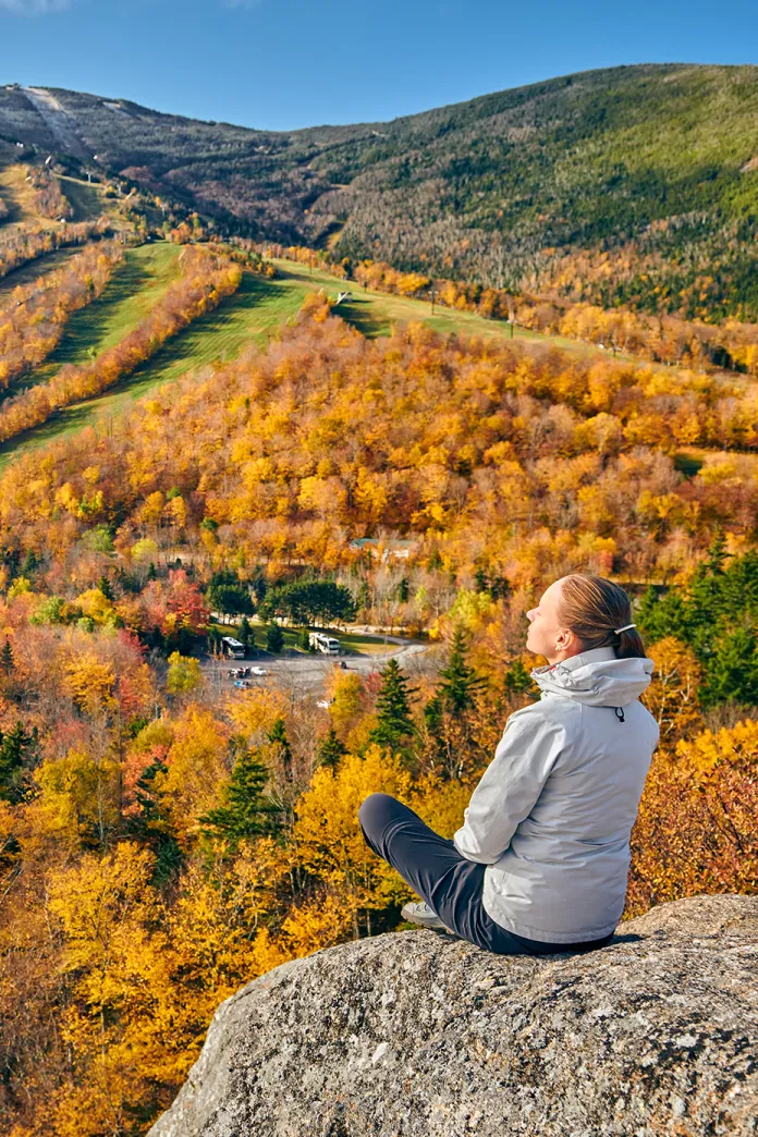 Person sitting on a rock overlooks bright yellow trees
