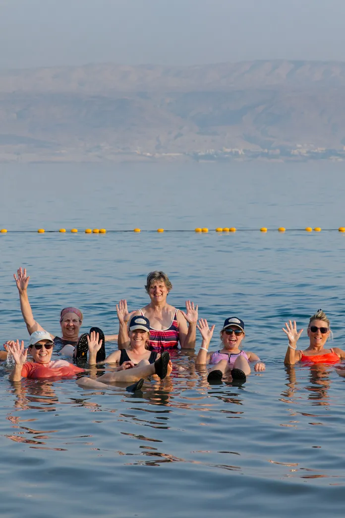 Group of smiling women waving while floating in the Dead Sea