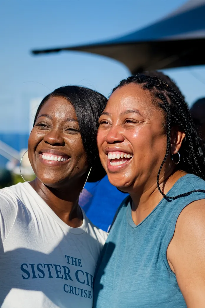 Two women laughing together for a selfie outdoors by the water