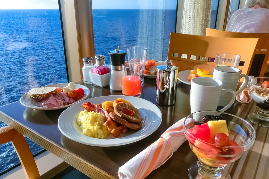 Table set with various breakfast foods and beverages next to a window overlooking the ocean.