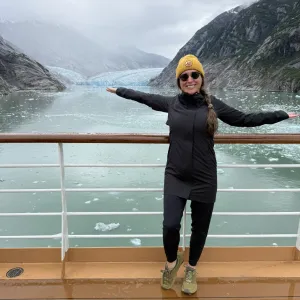 Smiling woman standing on the deck of a cruise ship with the ocean and mountains in the background