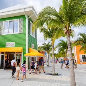 Green building with yellow awnings surrounded by palm trees and tourists walking around
