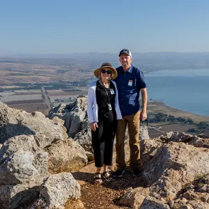 Smiling couple standing near a rocky click with an aerial view of Israel in the back ground