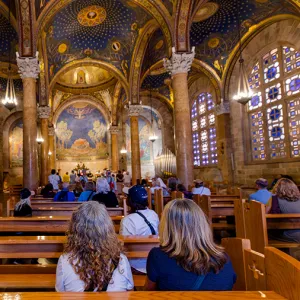 Visitors seated inside an ornate church with vaulted blue-and-gold ceilings, stone columns, and stained glass windows during a tour in Israel.