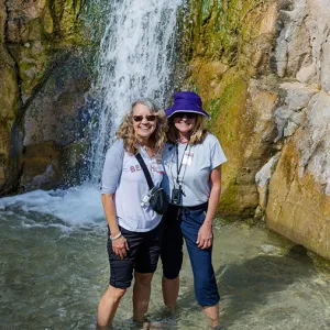 Two smiling women standing in front of a waterfall